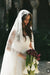 Elegant bride wearing a long lace wedding veil looking down at her bouquet with soft romantic bridal makeup by Karysha Beauty