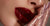Close-up of a person wearing red lipstick with a glittery lip gloss on a neutral background