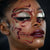 Close-up of a model's face featuring dramatic gothic makeup with metallic silver glitter eyeshadow, deep burgundy lipstick, and intricate red body paint and bead detailing around the eyes, nose, and mouth.