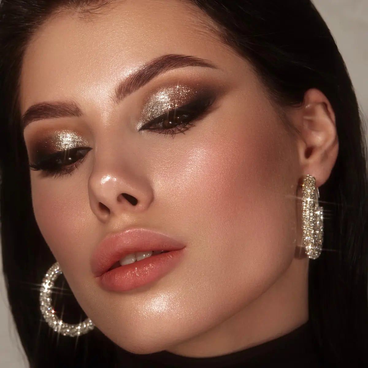 Close-up of a model featuring sparkling gold glitter eyeshadow, bold smokey eyeliner, and radiant skin