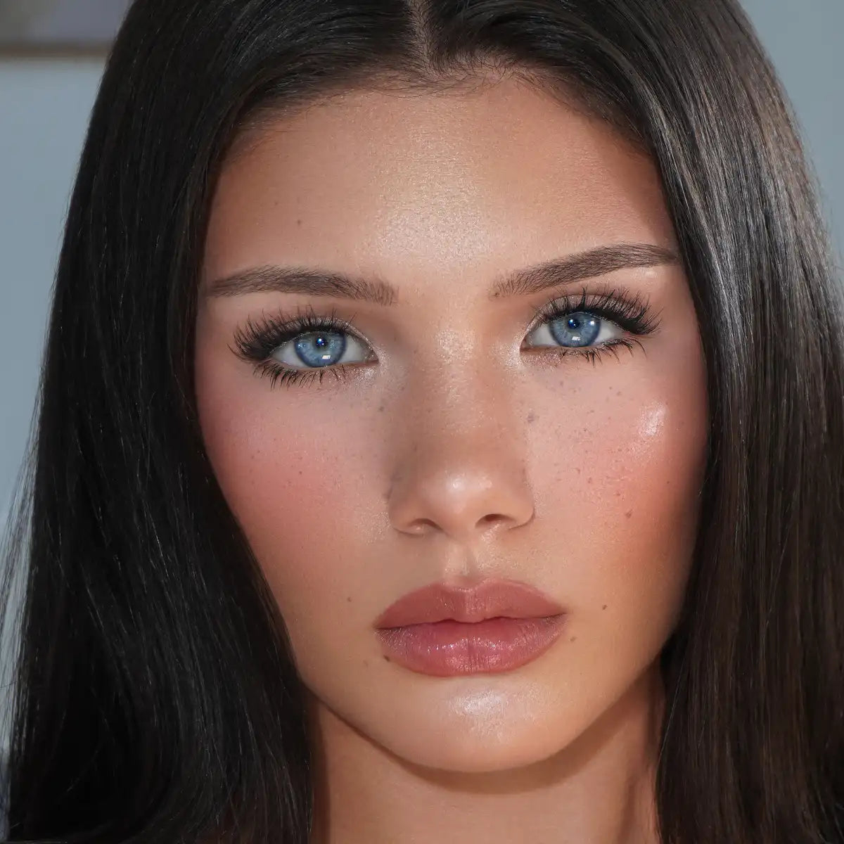 Stunning blue-eyed brunette with straight dark hair displaying natural glowing skin, long eyelashes, and nude lip makeup