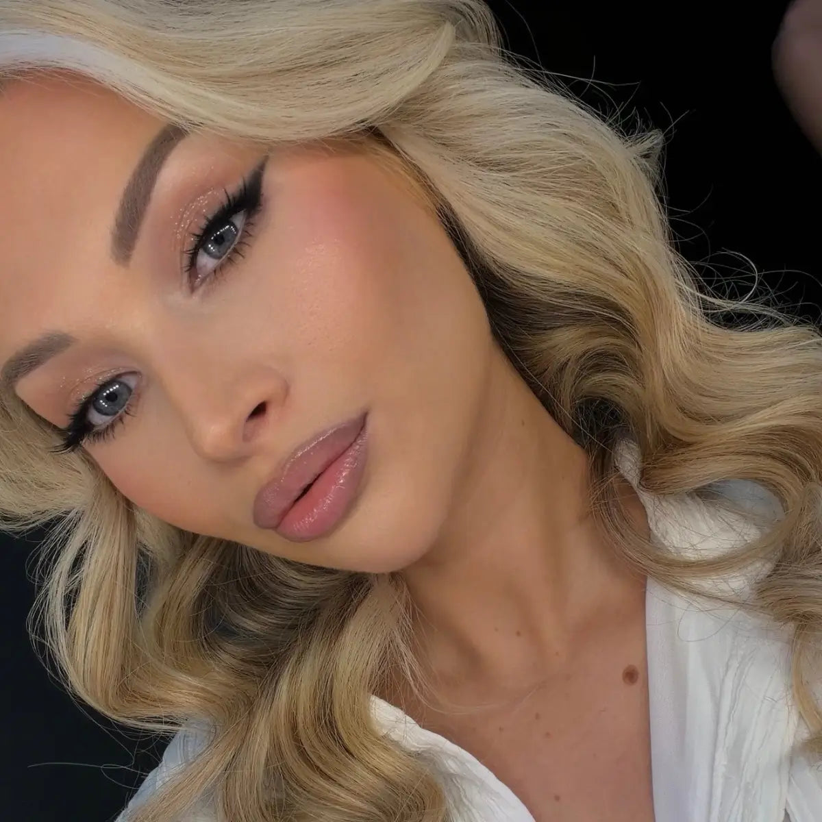 Blonde model showcasing dramatic black winged eyeliner, shimmering eyeshadow, and glossy nude lips