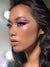 Close-up of a person with dramatic makeup, including purple eye shadow and long eyelashes.