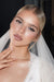 Close-up of a blonde bride touching her neck gently, showing off her glowing skin, winged eyeliner, and glossy nude lips by Karysha Beauty
