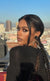 Woman with braided hair and makeup standing against a cityscape background