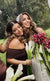 Happy bride holding a wedding bouquet hugging her bridesmaid, both featuring flawless professional wedding makeup by Karysha Beauty.